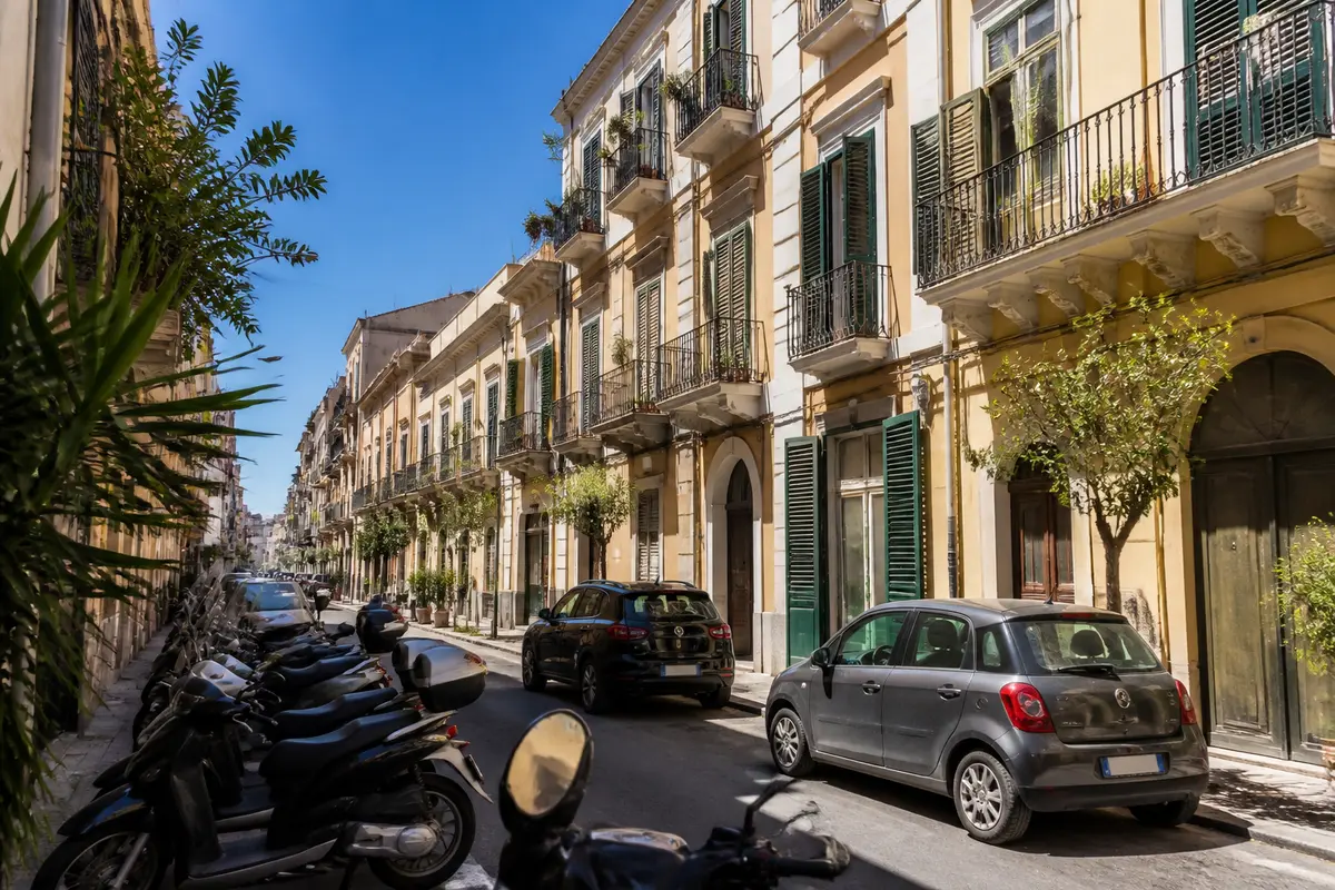 Strada cittadina con edifici storici e veicoli parcheggiati, scenario del mercato immobiliare italiano